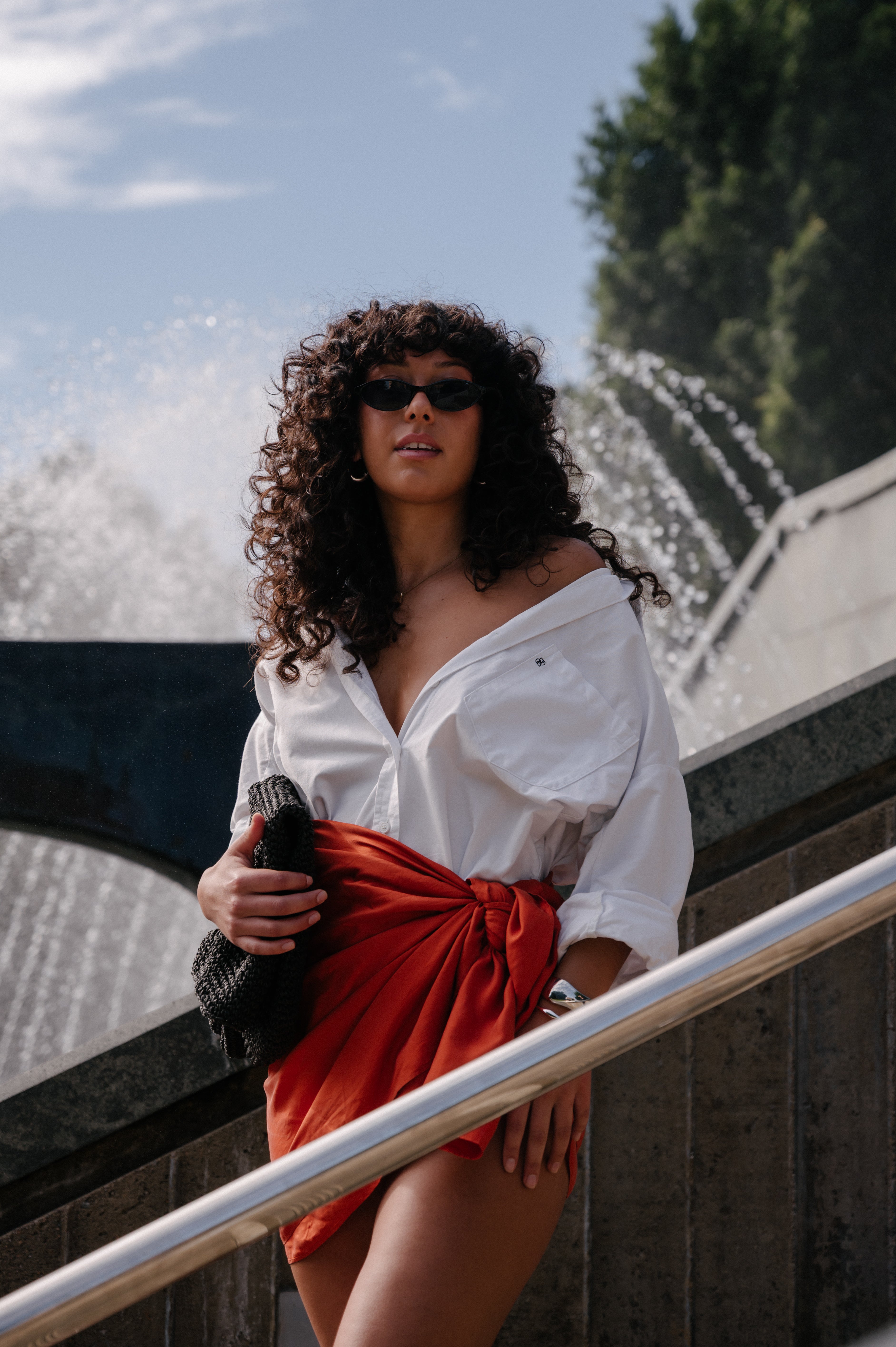 Woman in a white shirt and red skirt standing in front of a fountain