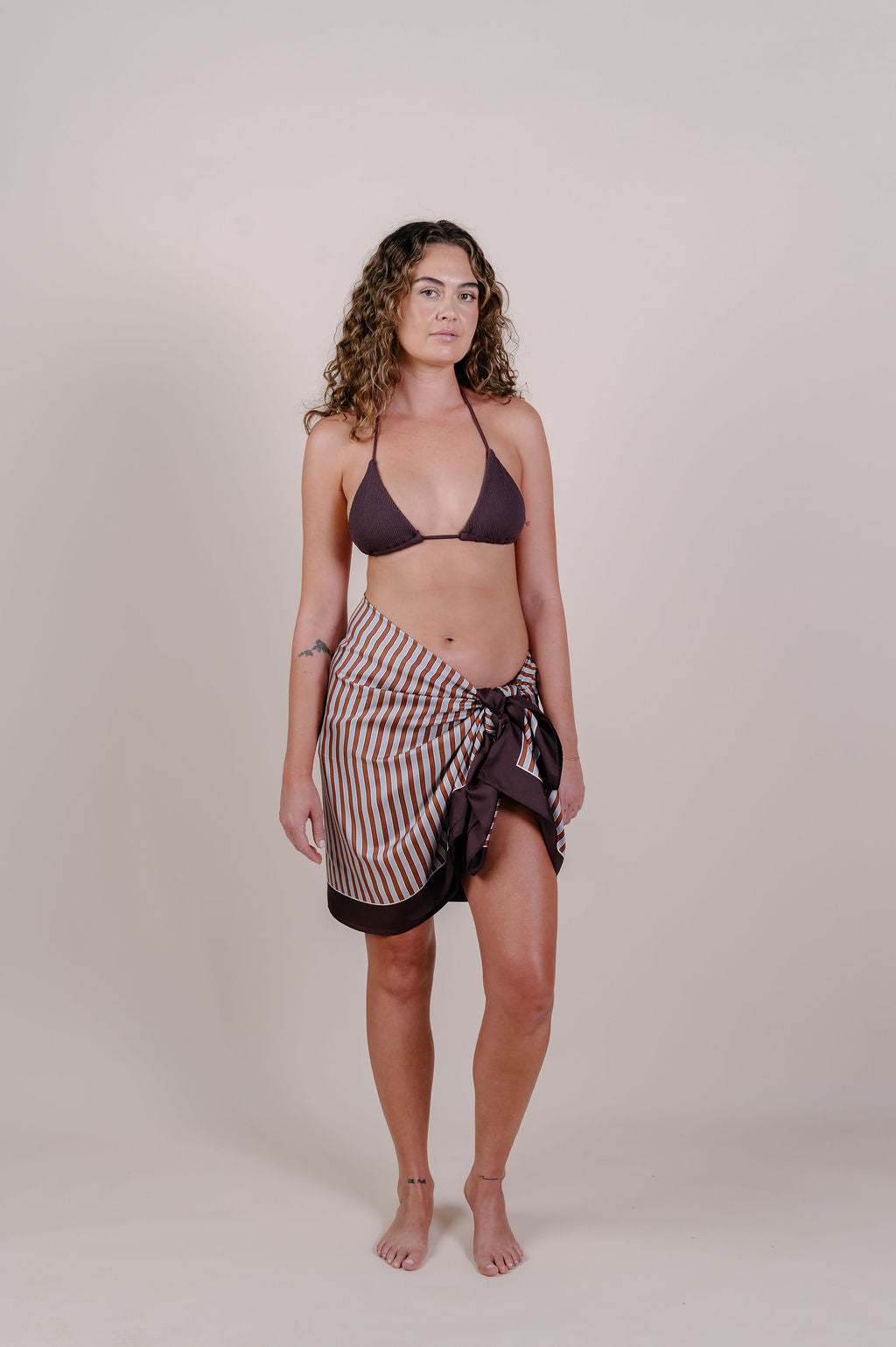 Model wearing the Amara clay stripe silk pareo by Novo Pareo. 100% Mulberry Silk Twill in warm clay and ivory tones, designed in Australia for refined resort wear from beach to beyond.