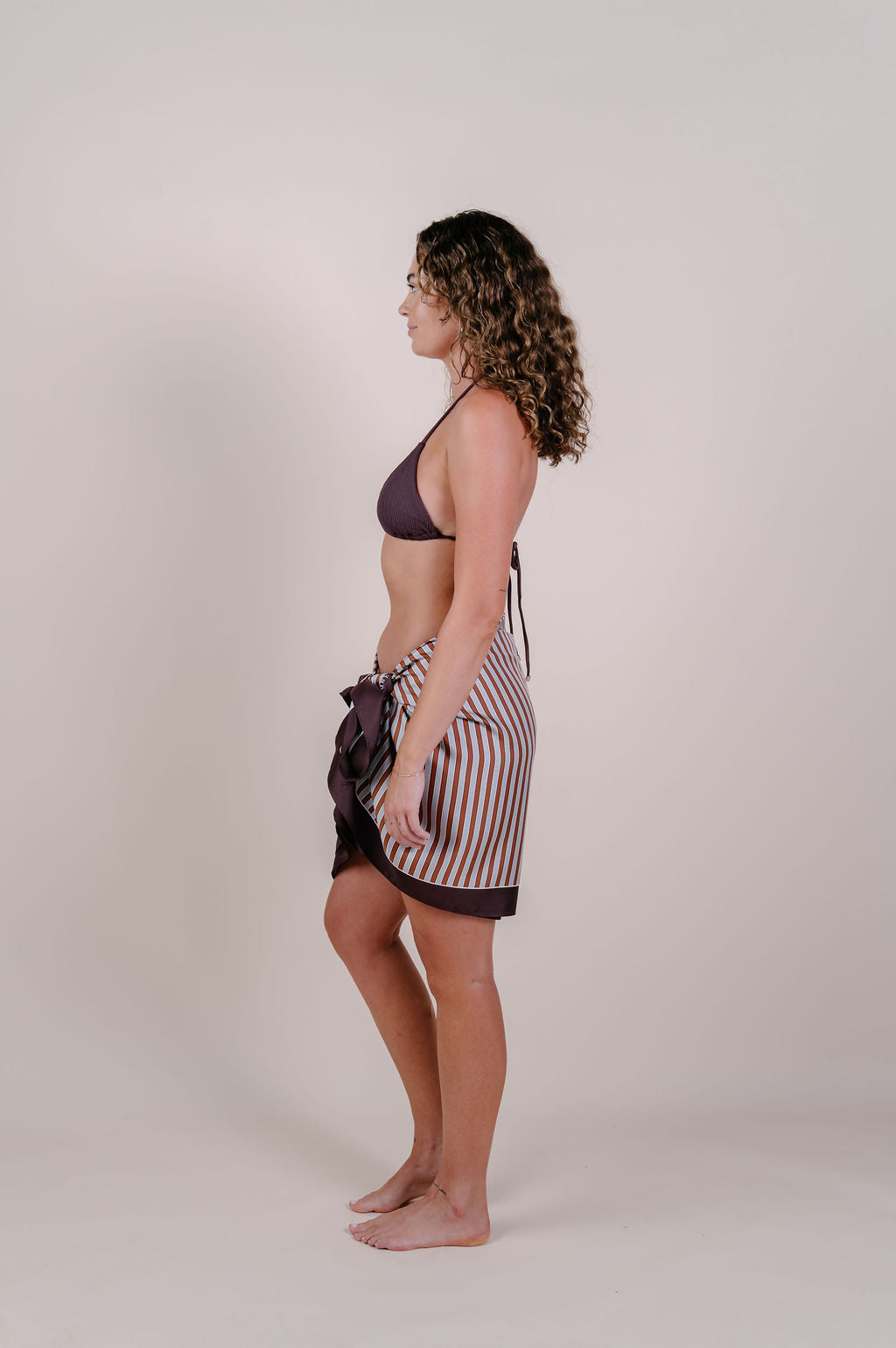 Model wearing the Amara clay stripe silk pareo by Novo Pareo. 100% Mulberry Silk Twill in warm clay and ivory tones, designed in Australia for refined resort wear from beach to beyond.