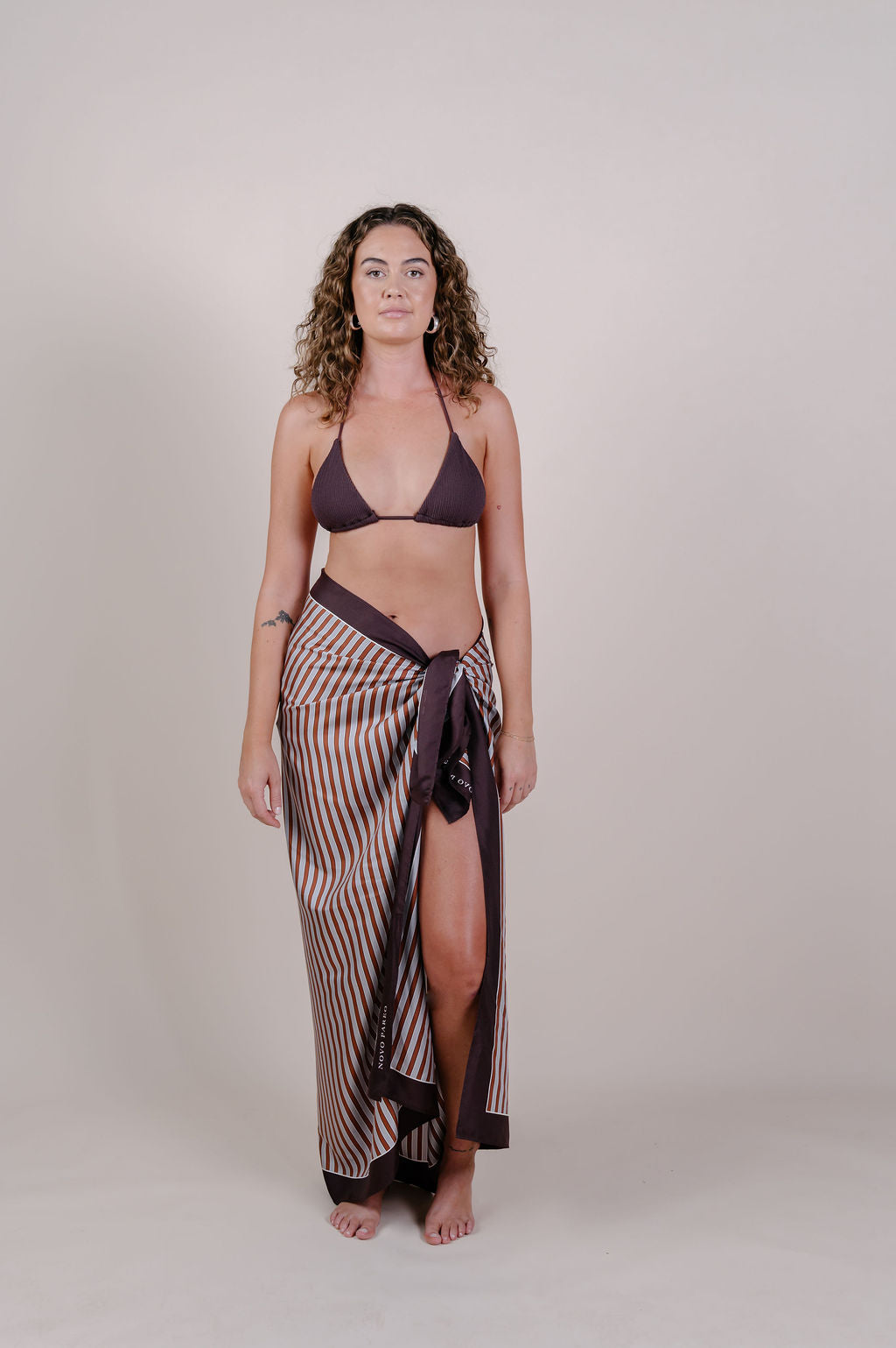 Model wearing the Amara clay stripe silk pareo by Novo Pareo. 100% Mulberry Silk Twill in warm clay and ivory tones, designed in Australia for refined resort wear from beach to beyond.
