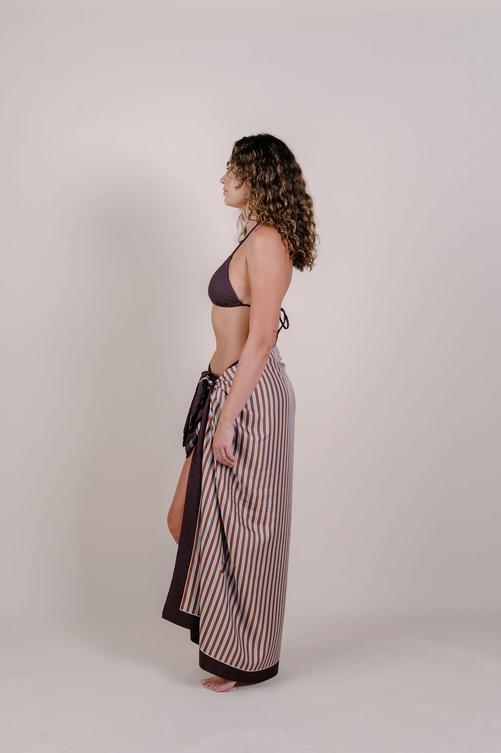 Model wearing the Amara clay stripe silk pareo by Novo Pareo. 100% Mulberry Silk Twill in warm clay and ivory tones, designed in Australia for refined resort wear from beach to beyond.