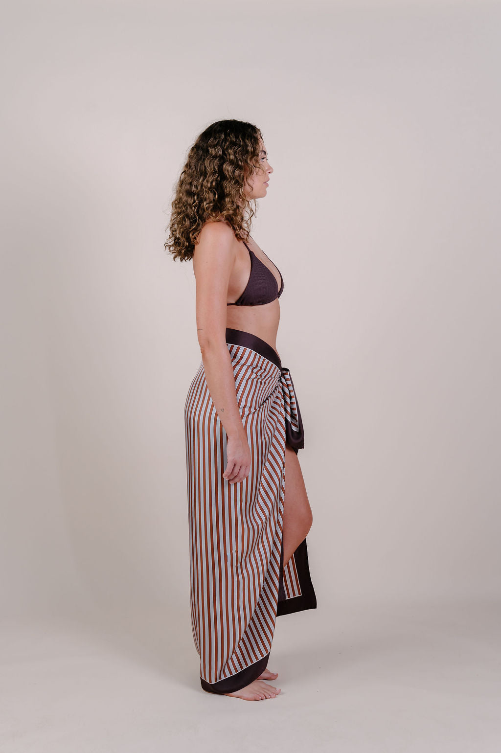 Model wearing the Amara clay stripe silk pareo by Novo Pareo. 100% Mulberry Silk Twill in warm clay and ivory tones, designed in Australia for refined resort wear from beach to beyond.