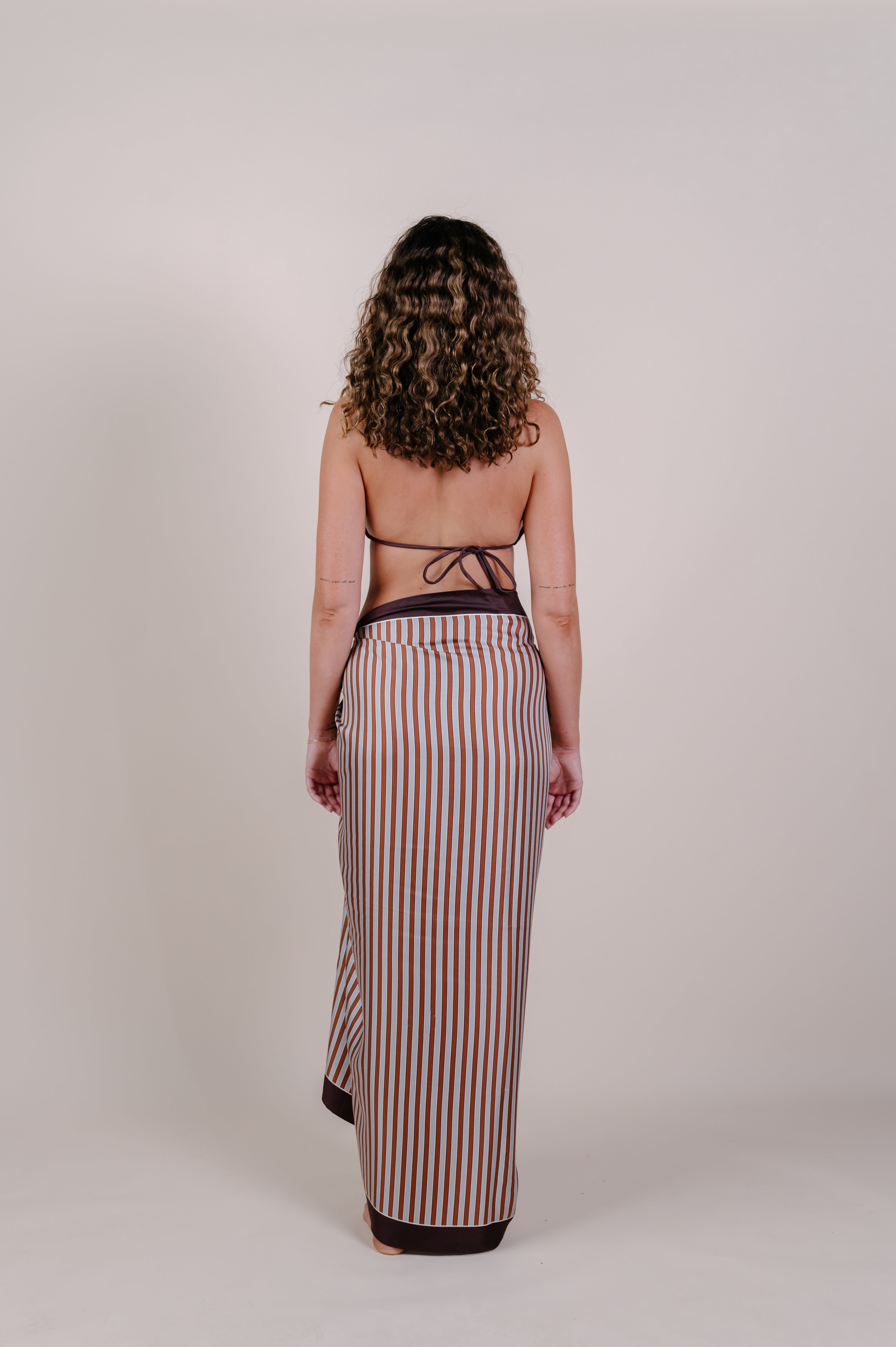 Model wearing the Amara clay stripe silk pareo by Novo Pareo. 100% Mulberry Silk Twill in warm clay and ivory tones, designed in Australia for refined resort wear from beach to beyond.