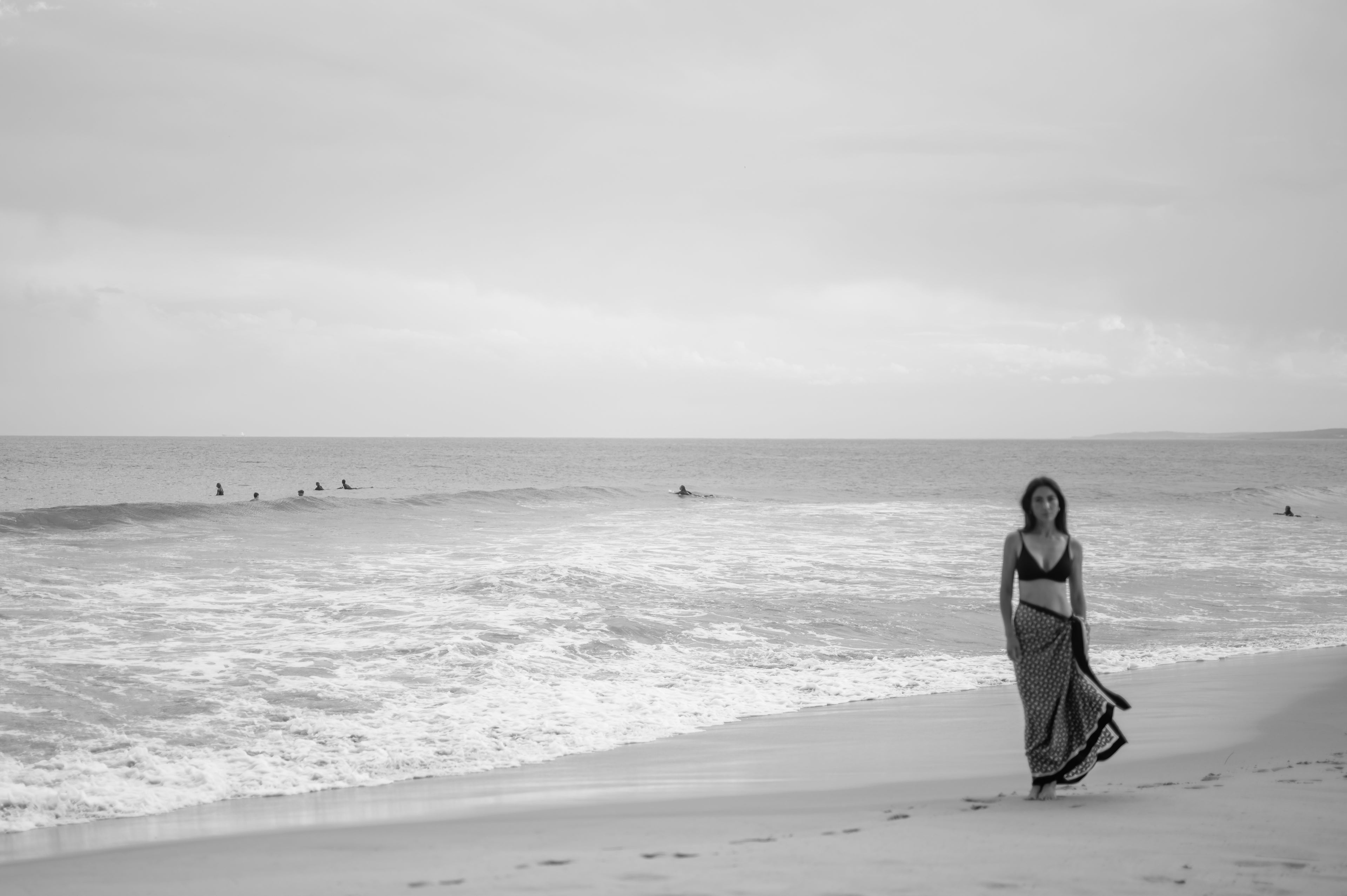 Woman walking on a beach with ocean waves and a cloudy sky.