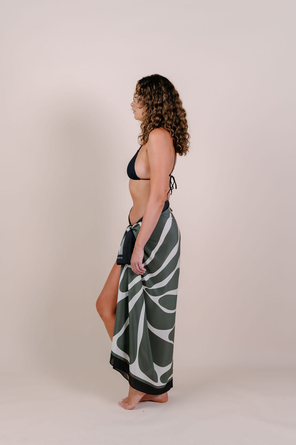Model wearing the Camille olive abstract silk pareo by Novo Pareo. 100% Mulberry Silk Twill with flowing organic lines, designed in Australia for effortless, refined resort wear versatility.