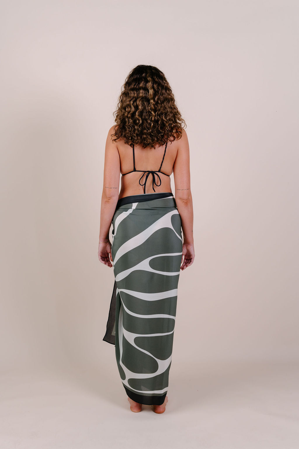 Model wearing the Camille olive abstract silk pareo by Novo Pareo. 100% Mulberry Silk Twill with flowing organic lines, designed in Australia for effortless, refined resort wear versatility.