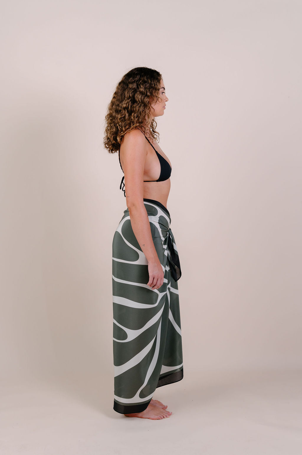 Model wearing the Camille olive abstract silk pareo by Novo Pareo. 100% Mulberry Silk Twill with flowing organic lines, designed in Australia for effortless, refined resort wear versatility.