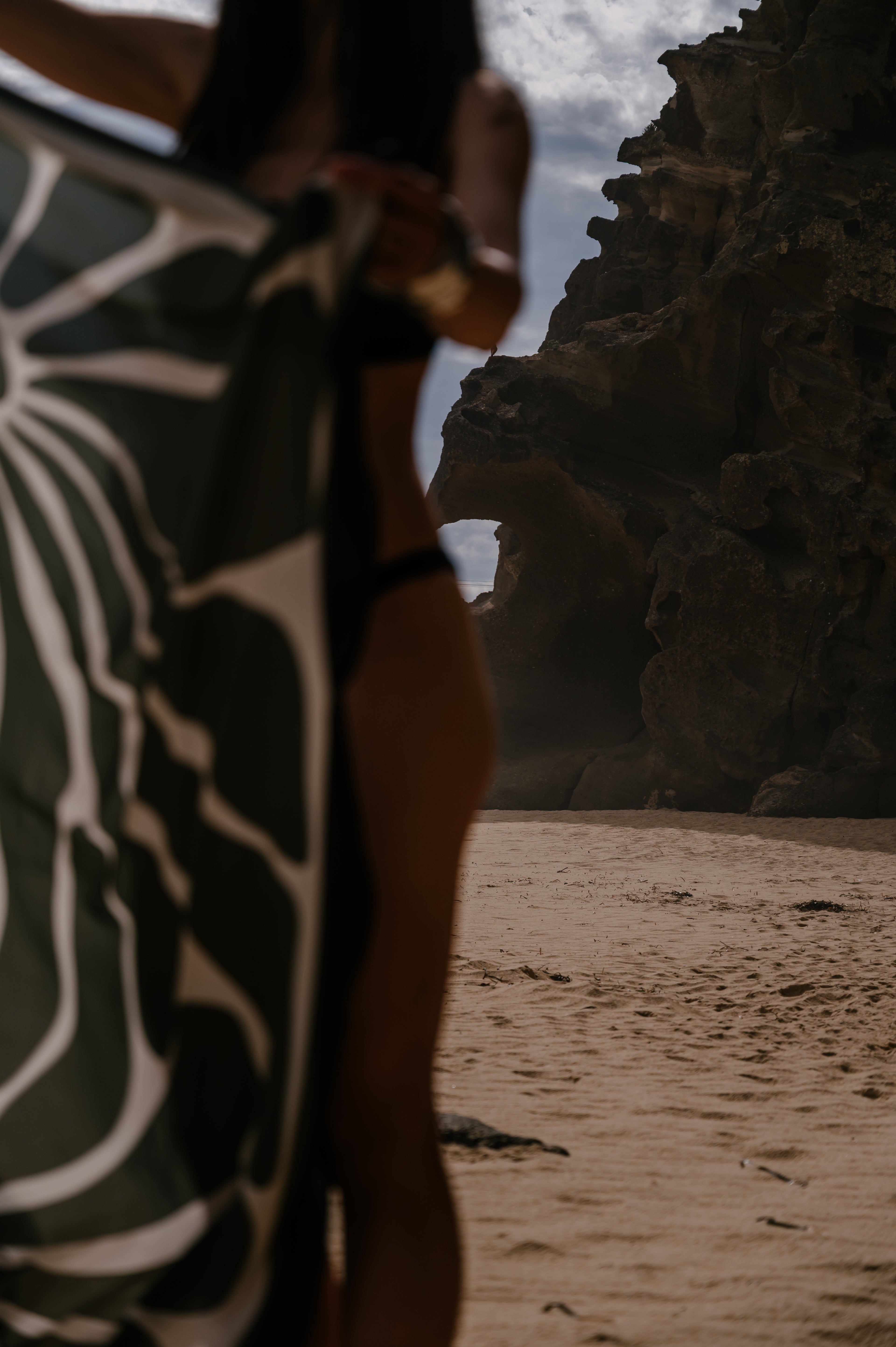 Person wearing a patterned pareo sarong on a beach with rocky cliffs in the background