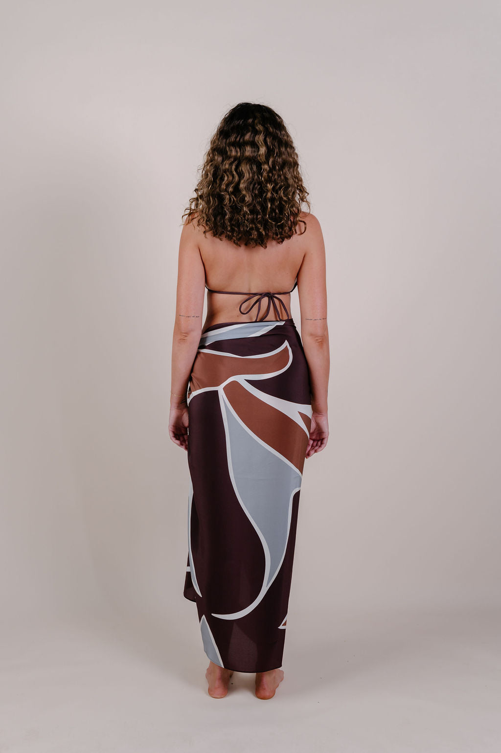 Model wearing the Isla flow print silk pareo by Novo Pareo. Elegant abstract design in deep chocolate and soft grey, crafted from 100% Mulberry Silk Twill for effortless, versatile resort wear.