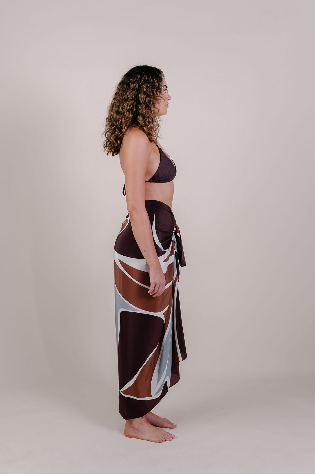 Model wearing the Isla flow print silk pareo by Novo Pareo. Elegant abstract design in deep chocolate and soft grey, crafted from 100% Mulberry Silk Twill for effortless, versatile resort wear.