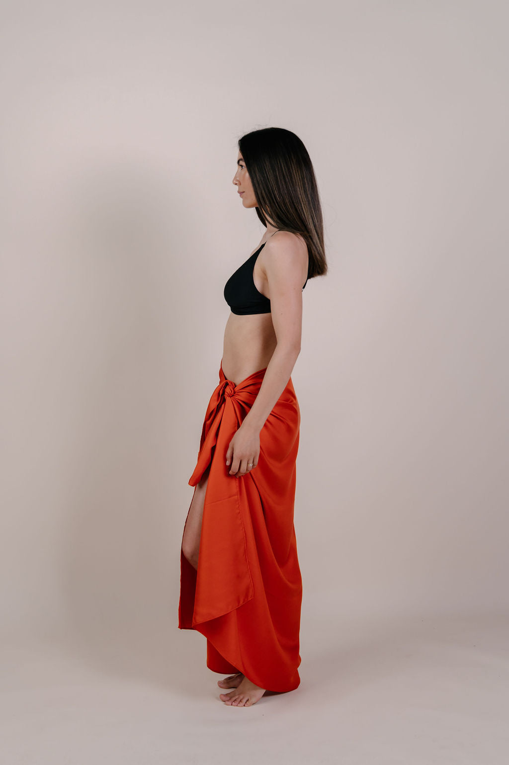 Model wearing the Luana solid terracotta silk pareo by Novo Pareo. Made from 100% Mulberry Silk Twill in warm terracotta, a timeless and versatile piece for refined Australian resort wear.