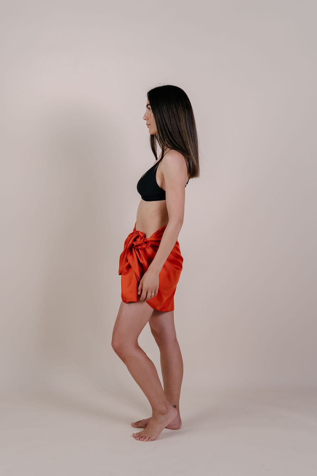 Model wearing the Luana solid terracotta silk pareo by Novo Pareo. Made from 100% Mulberry Silk Twill in warm terracotta, a timeless and versatile piece for refined Australian resort wear.