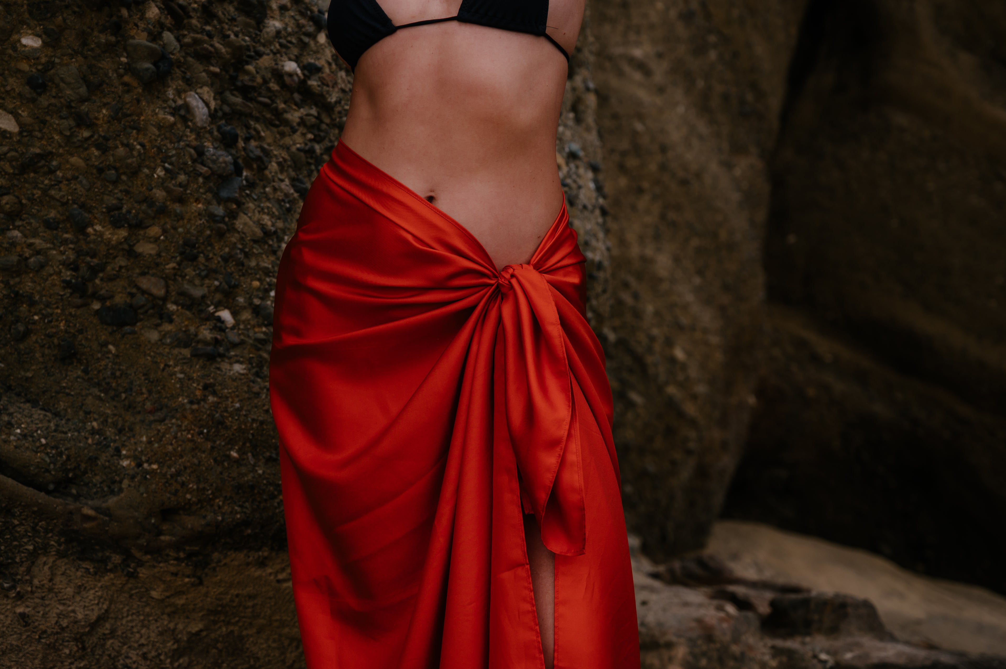 Person wearing a red sarong and black bikini top against a natural background