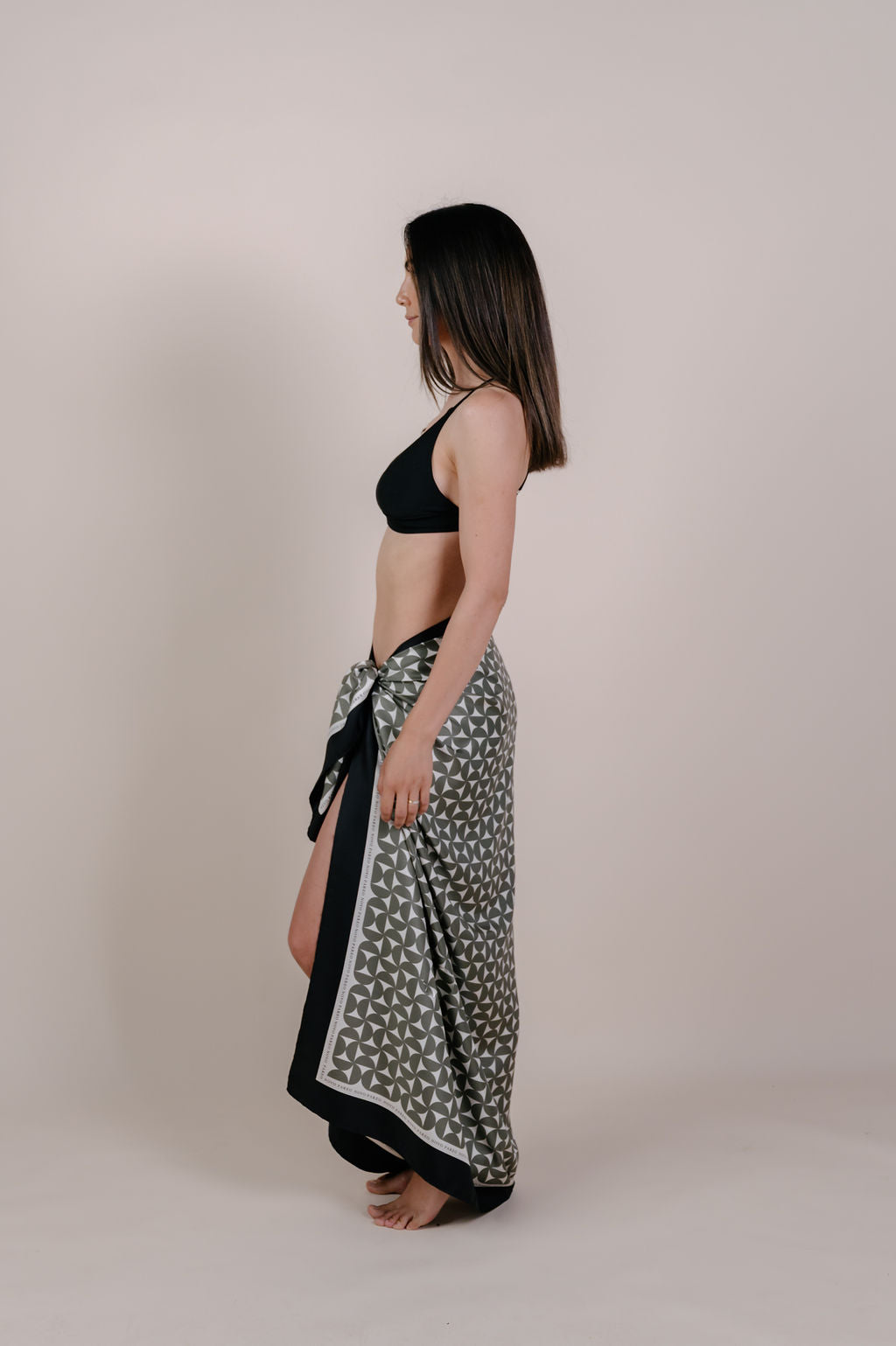 Model wearing the Solenne olive geometric silk pareo by Novo Pareo. 100% Mulberry Silk Twill with timeless geometric design and contrast border, created for refined Australian resort wear from beach to beyond.