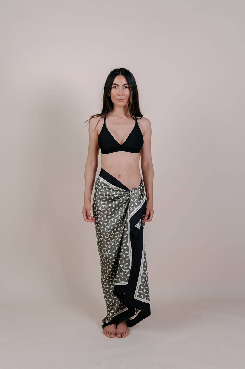 Model wearing the Solenne olive geometric silk pareo by Novo Pareo. 100% Mulberry Silk Twill with timeless geometric design and contrast border, created for refined Australian resort wear from beach to beyond.
