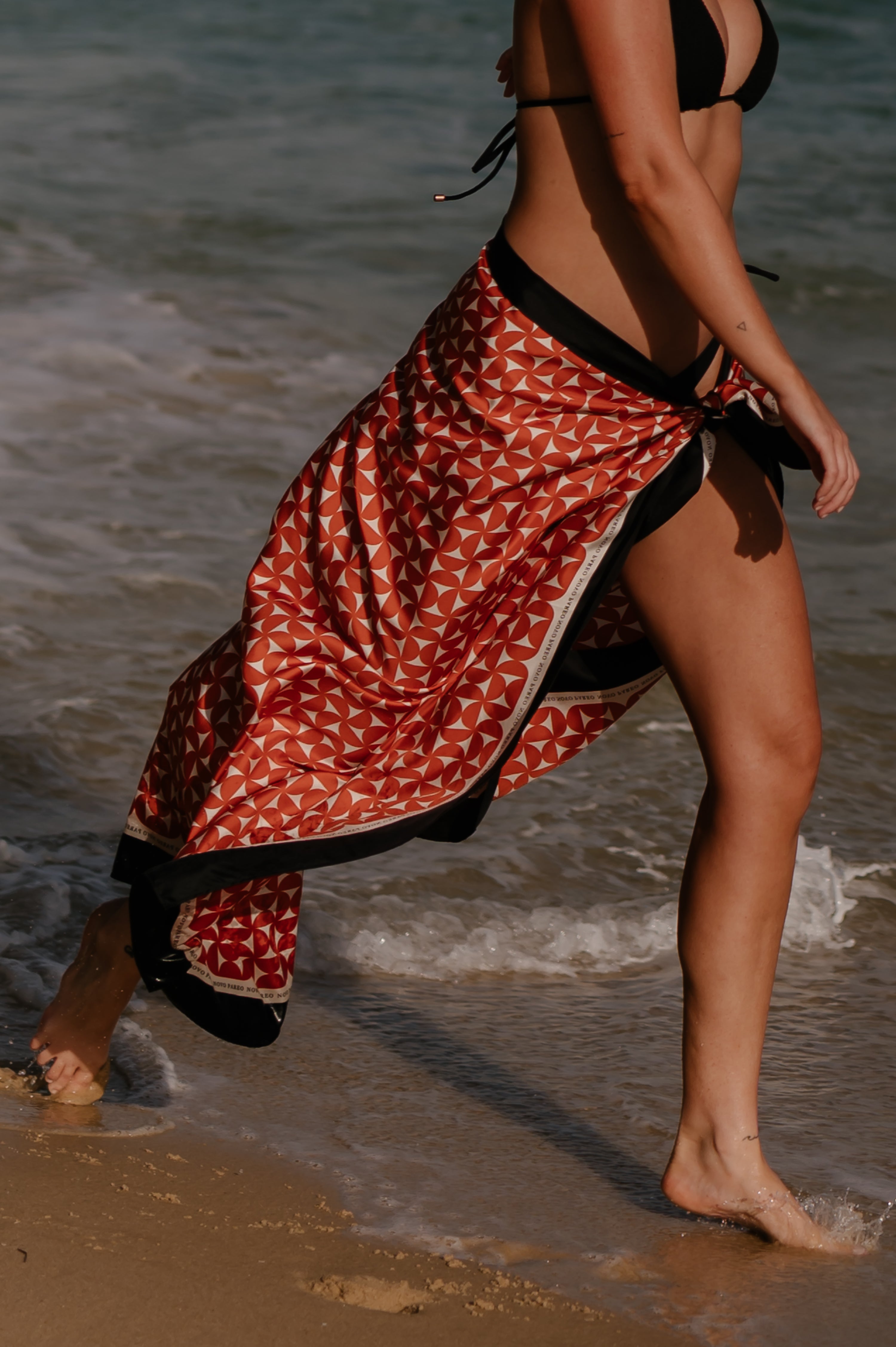 Person walking on a beach with a red and black patterned pareo sarong