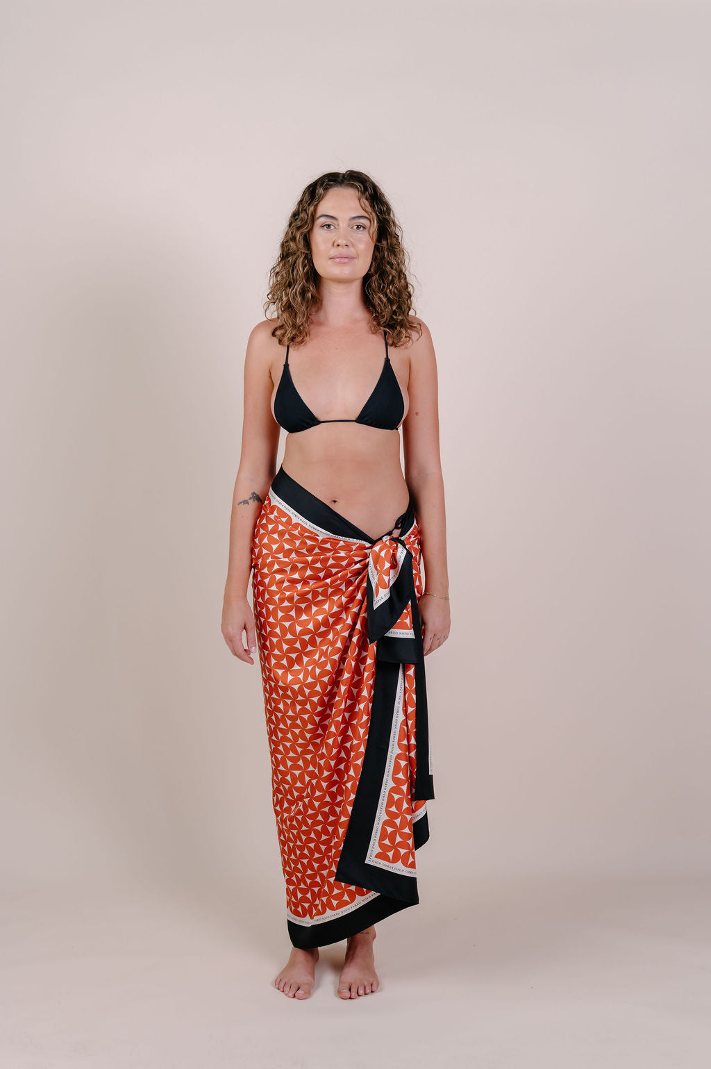 Model wearing the Sienna terracotta geometric silk pareo by Novo Pareo. 100% Mulberry Silk Crepe with bold terracotta print and contrast edge, designed in Australia for refined, timeless resort wear.