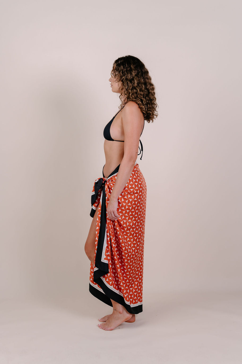 Model wearing the Sienna terracotta geometric silk pareo by Novo Pareo. 100% Mulberry Silk Crepe with bold terracotta print and contrast edge, designed in Australia for refined, timeless resort wear.