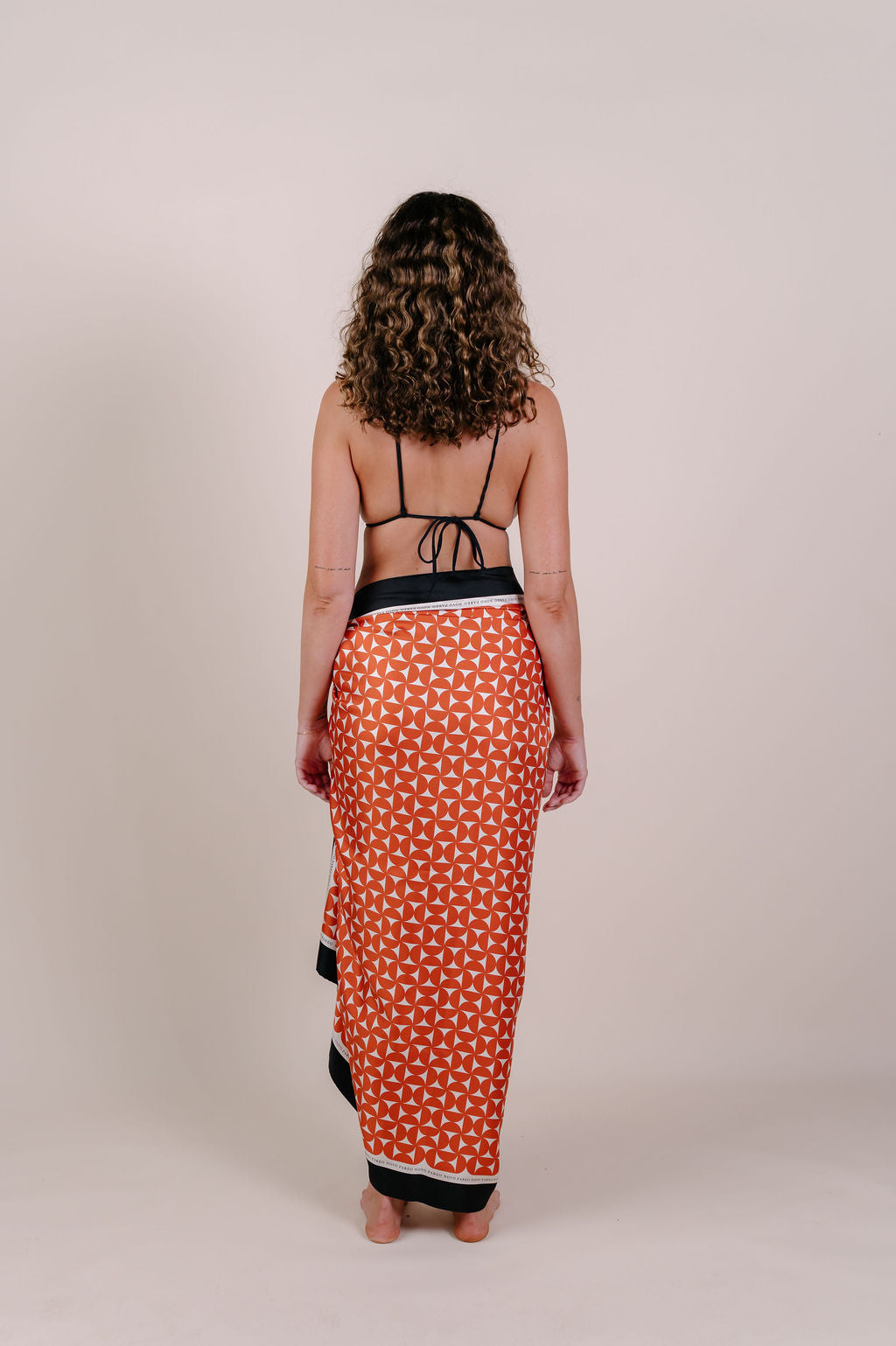 Model wearing the Sienna terracotta geometric silk pareo by Novo Pareo. 100% Mulberry Silk Crepe with bold terracotta print and contrast edge, designed in Australia for refined, timeless resort wear.