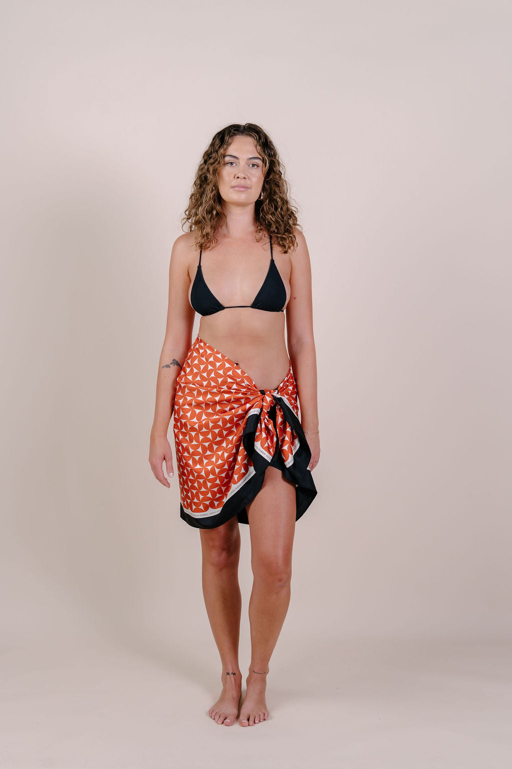 Model wearing the Sienna terracotta geometric silk pareo by Novo Pareo. 100% Mulberry Silk Crepe with bold terracotta print and contrast edge, designed in Australia for refined, timeless resort wear.