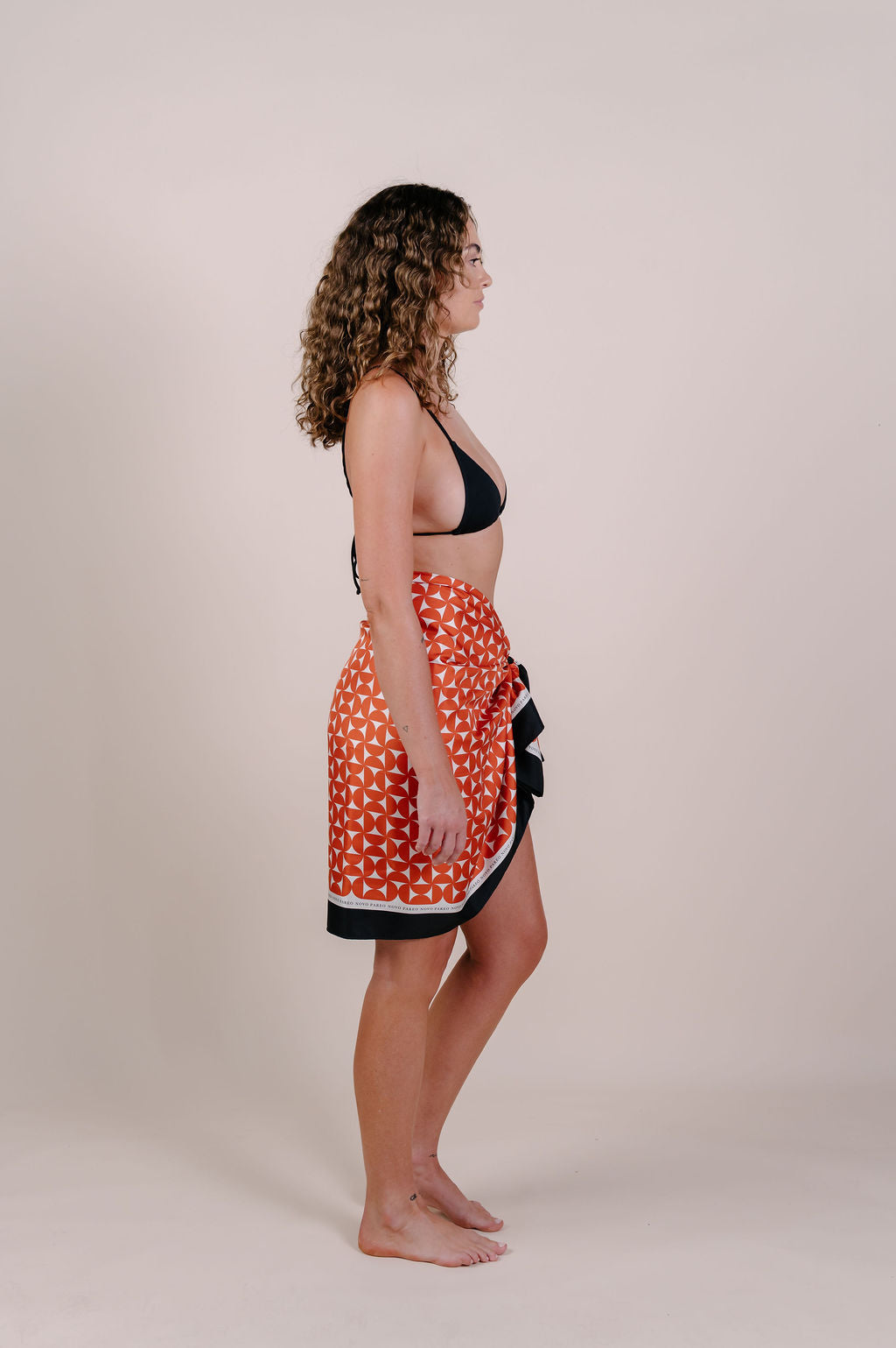 Model wearing the Sienna terracotta geometric silk pareo by Novo Pareo. 100% Mulberry Silk Crepe with bold terracotta print and contrast edge, designed in Australia for refined, timeless resort wear.