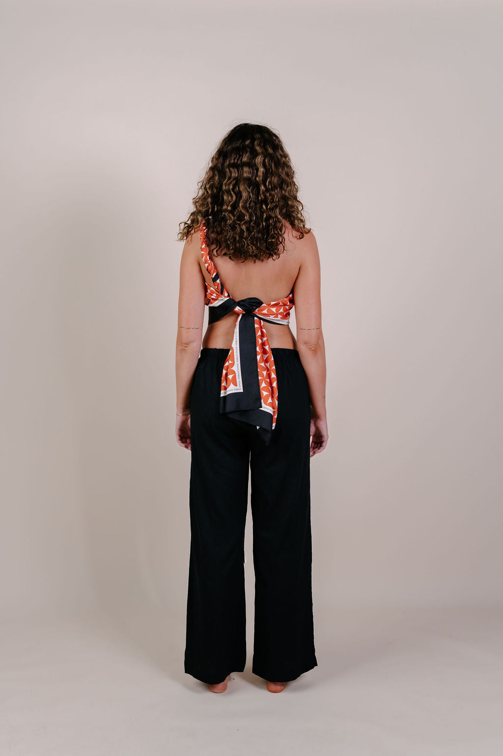 Model wearing the Sienna terracotta geometric silk pareo by Novo Pareo. 100% Mulberry Silk Crepe with bold terracotta print and contrast edge, designed in Australia for refined, timeless resort wear.